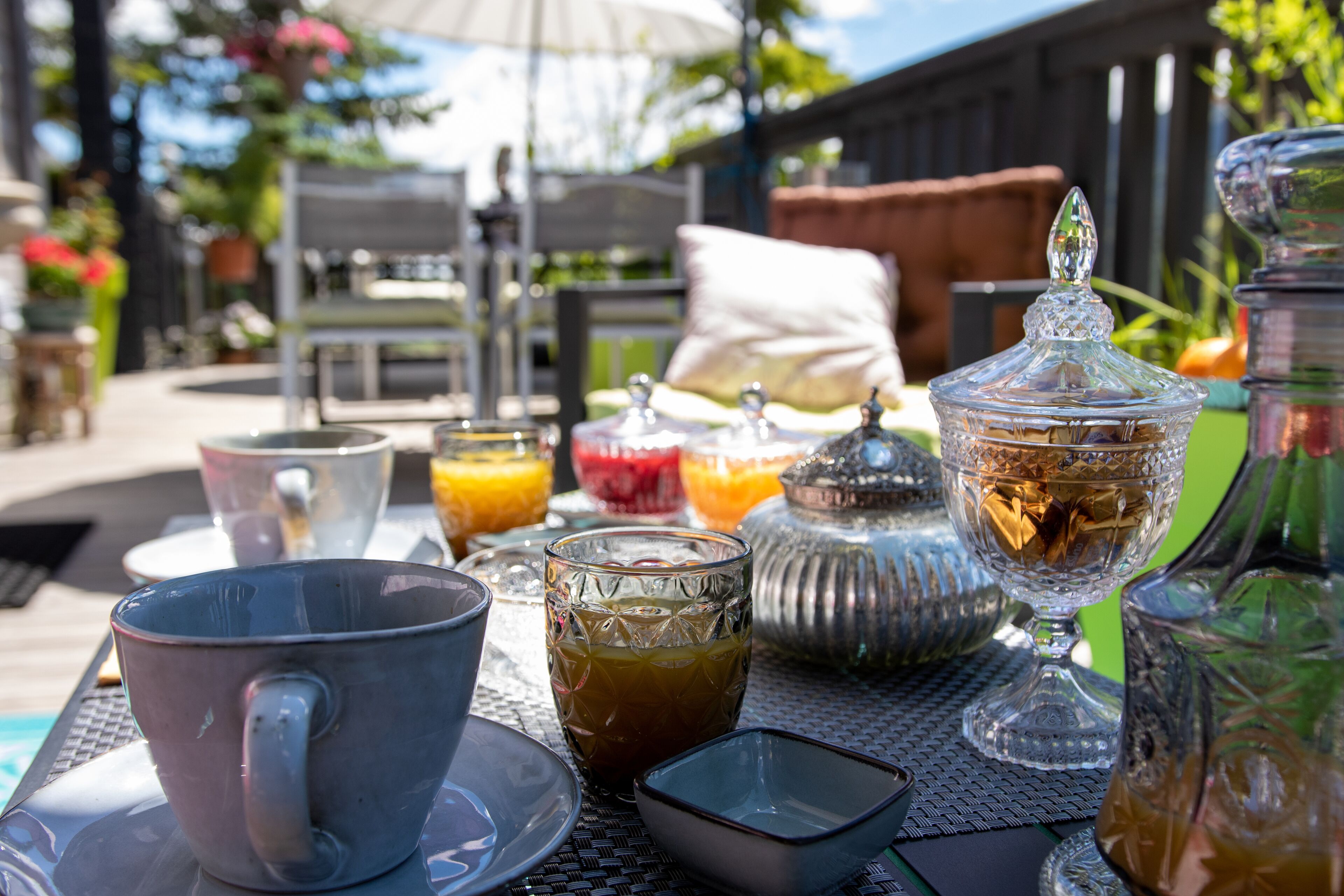A table set outdoors with various glassware, a pitcher, and a sugar bowl.