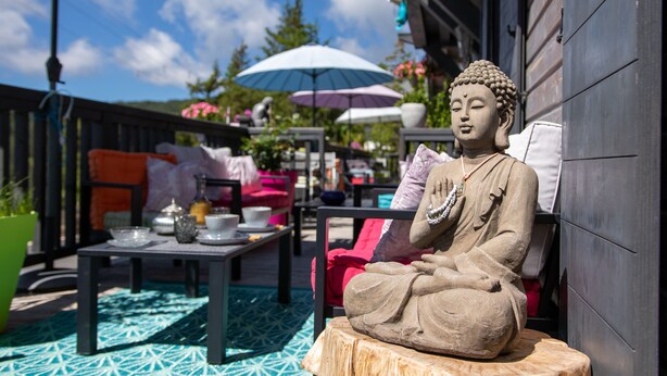 A Buddha statue in a garden setting with outdoor furniture and umbrellas. - Lalpen Roc (Caille)
