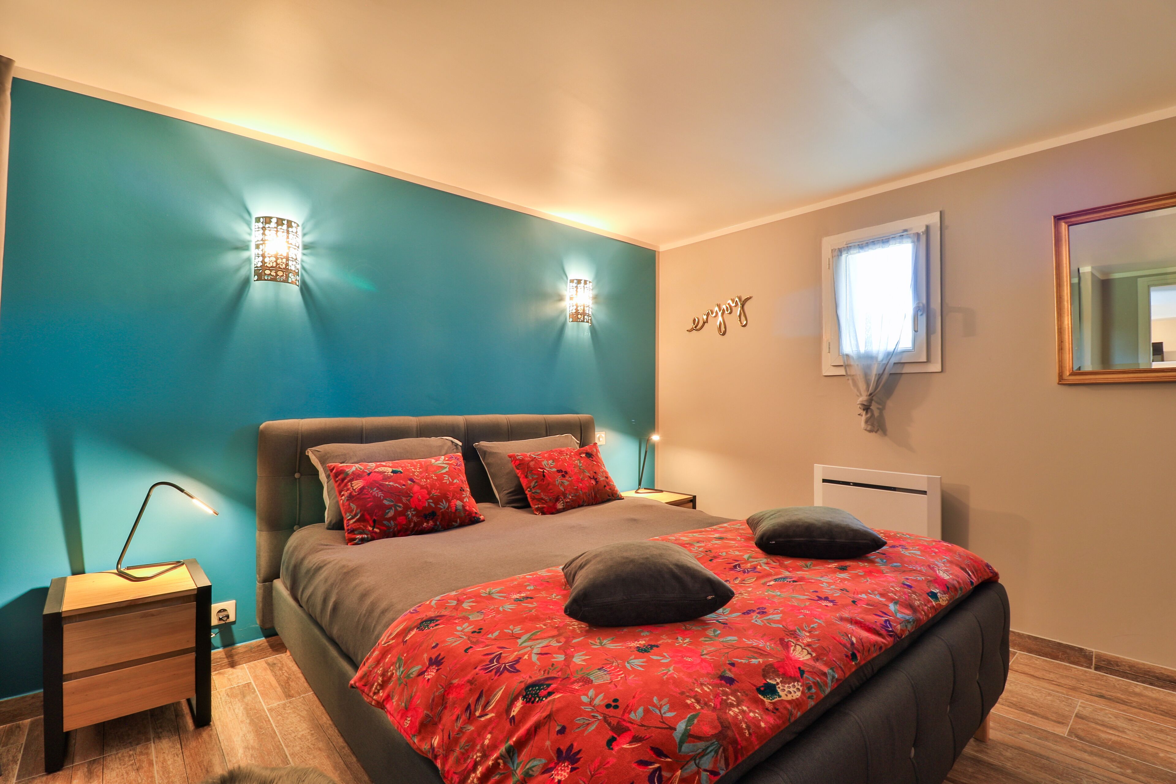 A bedroom with a bed, two wall sconces, a bedside table, a window with a view, and a mirror on the wall.