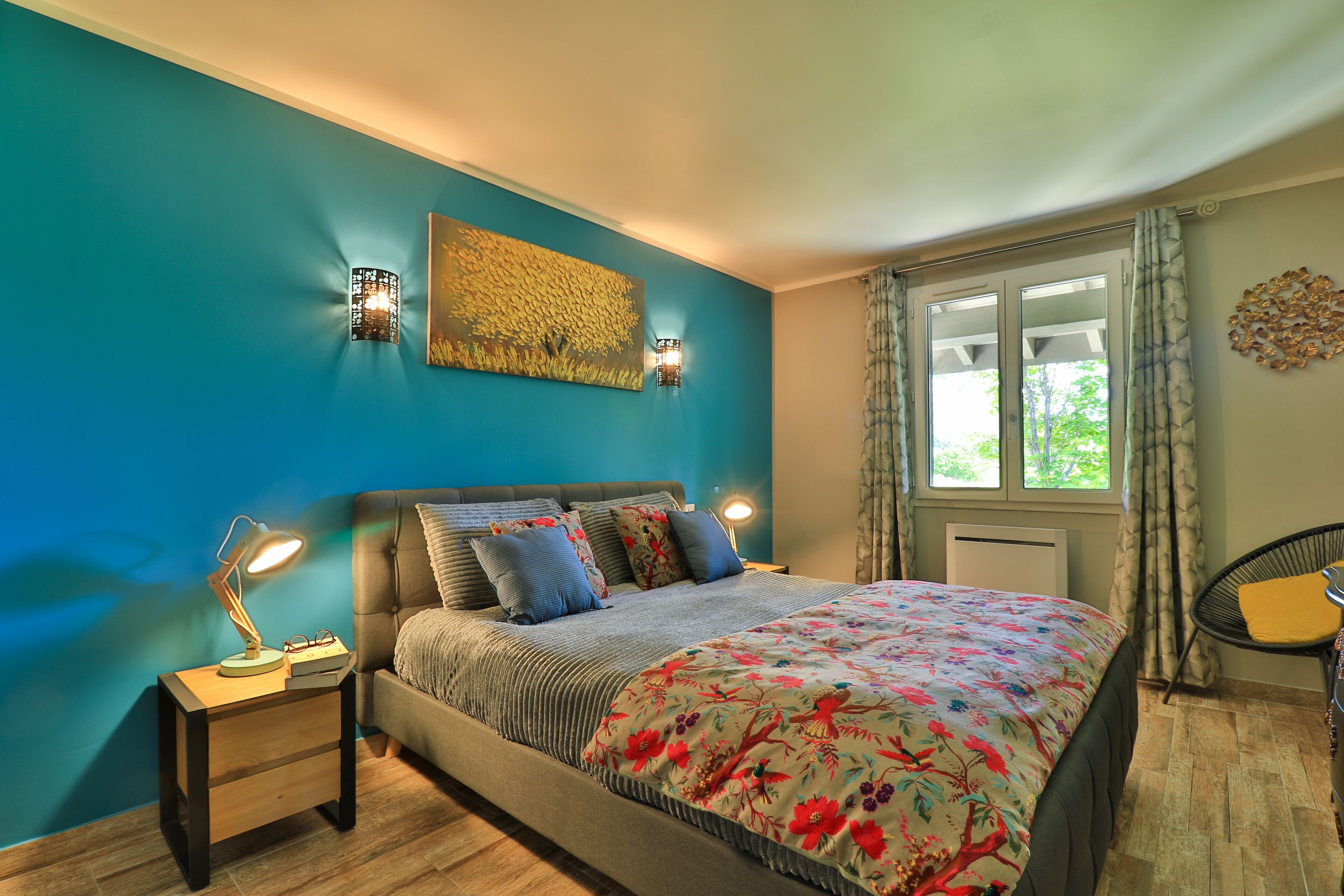Un dormitorio con cama, mesita de noche, decoración en la pared y una ventana con cortinas.