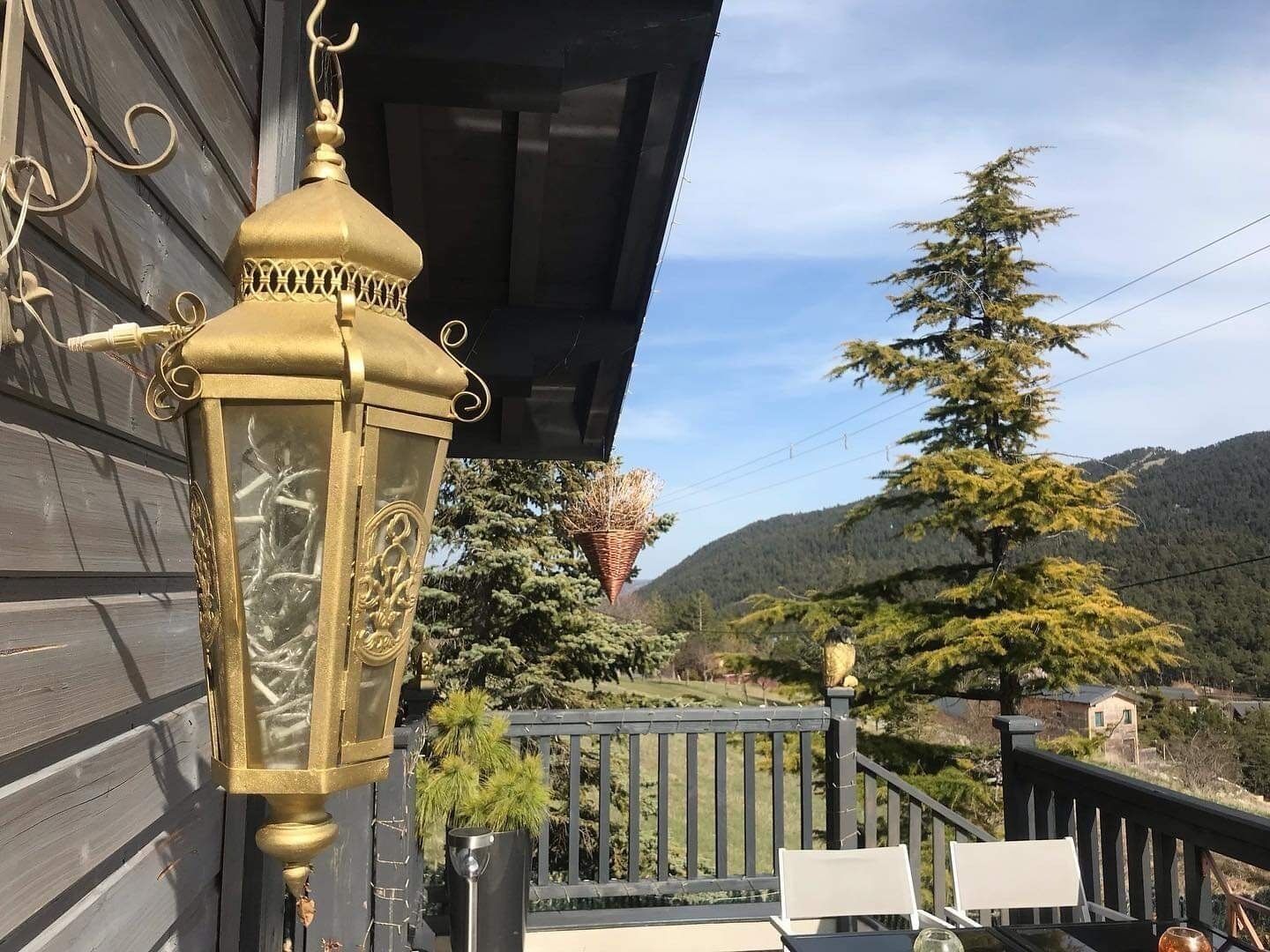 A balcony with a decorative lantern, a chair, and a view of a forested mountain.