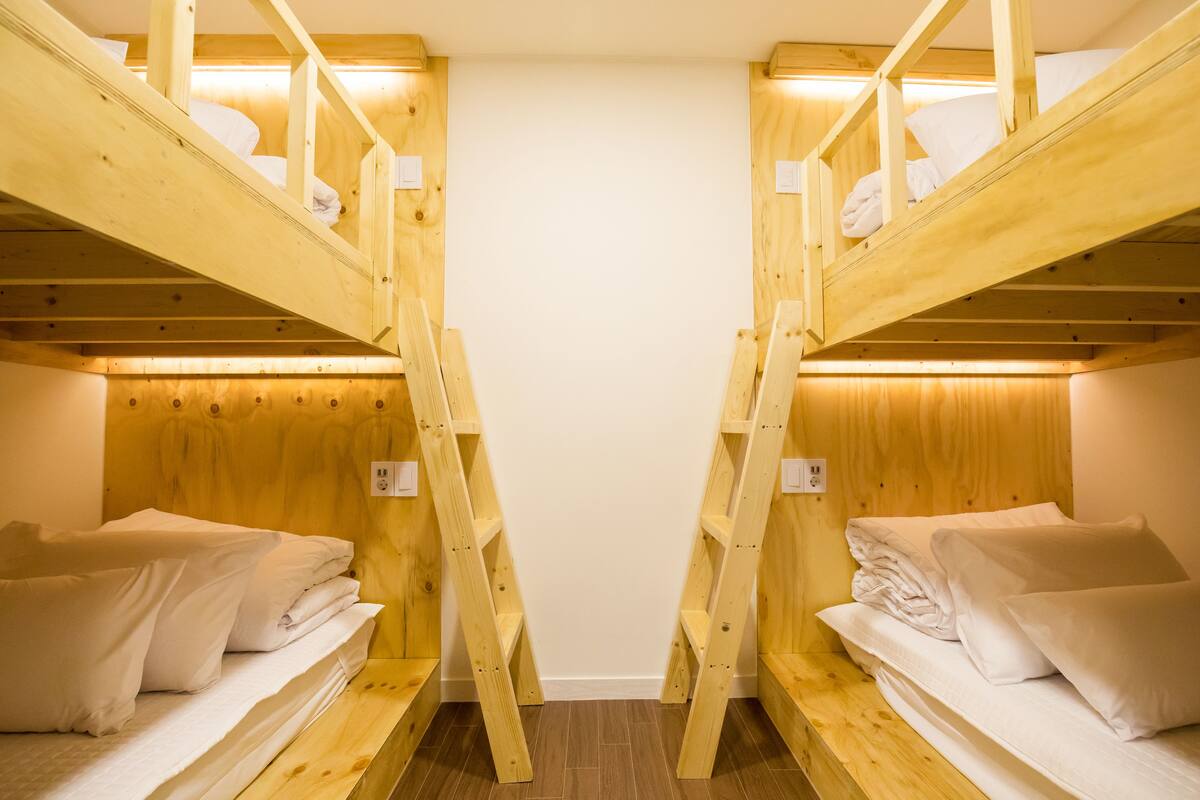 Una habitación con dos literas de madera, cada una con colchón y almohadas, y una escalera para subir.
