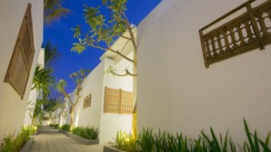 A narrow pathway flanked by white walls and wooden shutters, leading to a building entrance. - Bajra Bali Villa (Seminyak)