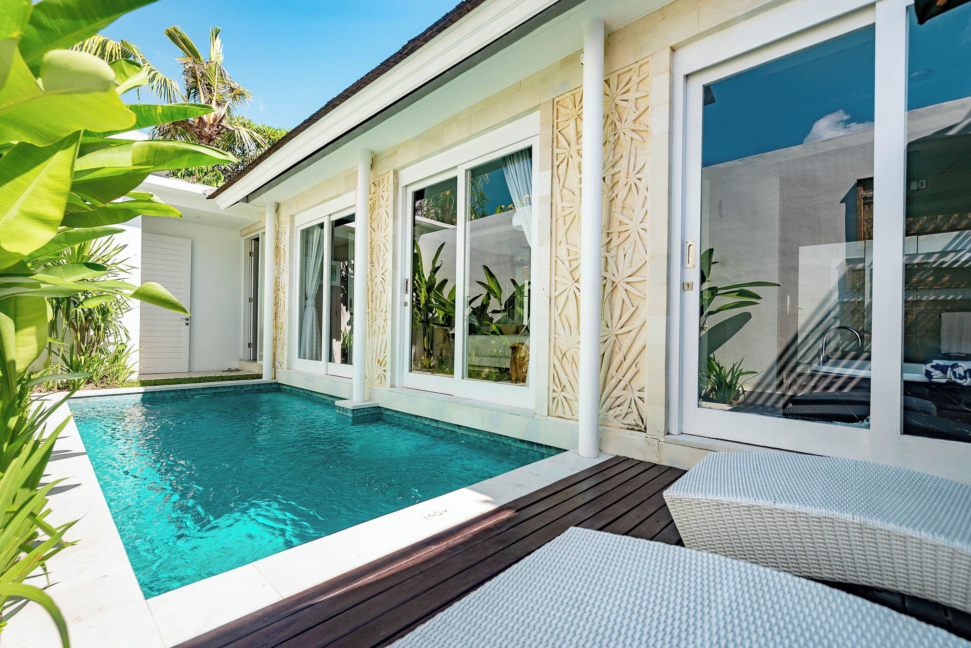 A swimming pool with a wooden deck, white walls, and large windows.