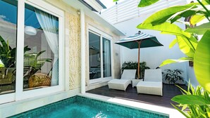 A poolside area with a clear blue pool, white wicker lounge chairs, and a large umbrella providing shade. - Bajra Bali Villa (Seminyak)