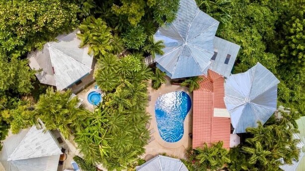 An aerial view of a resort with multiple umbrella-style structures, a swimming pool, and lush greenery. - Hotel Tamarindo Village (Tamarindo)