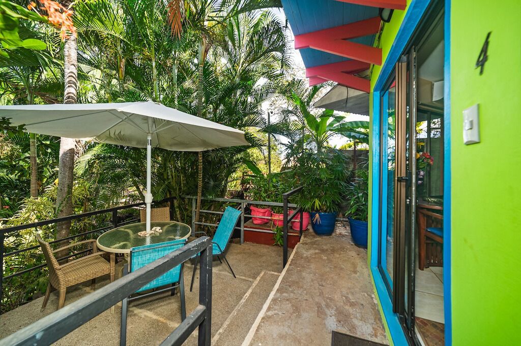 A balcony with a table and chairs, surrounded by potted plants and a large umbrella.