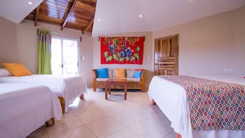 Una habitación de hotel con dos camas, un sofá, una mesa y un tapiz colorido.