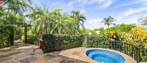 Un'area piscina con solarium piastrellato, immersa nel verde e circondata da palme.