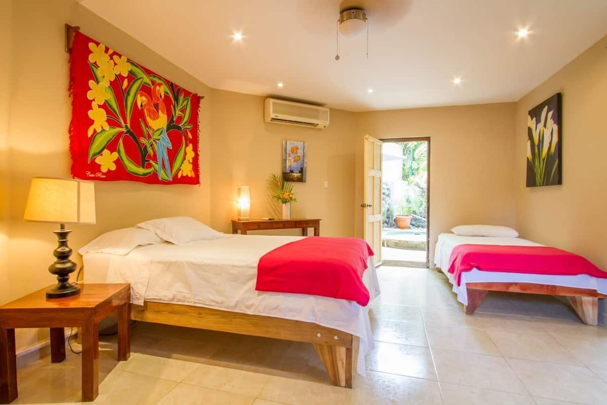 A hotel room with two beds, a red tapestry, a lamp, and a door leading to a balcony.