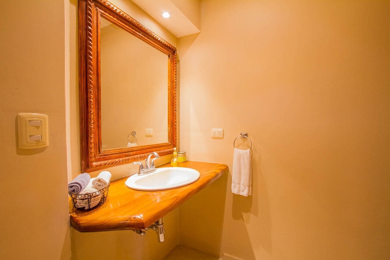 A bathroom with a wooden vanity, a white sink, a large mirror, a towel rack, and a basket of towels.