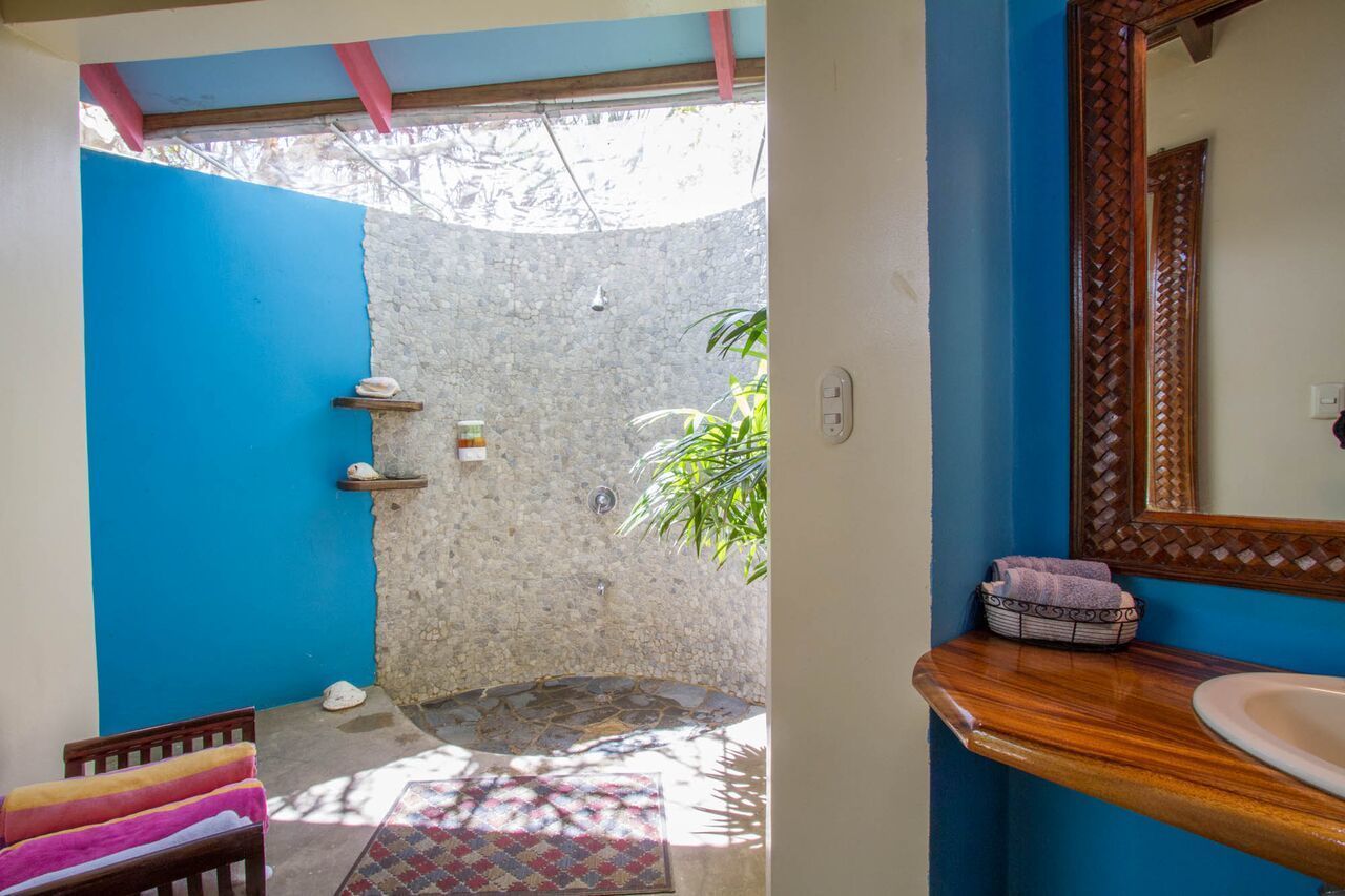 Une salle de bain avec un mur bleu, un meuble-lavabo en bois, un miroir et un espace douche avec un mur en pierre.