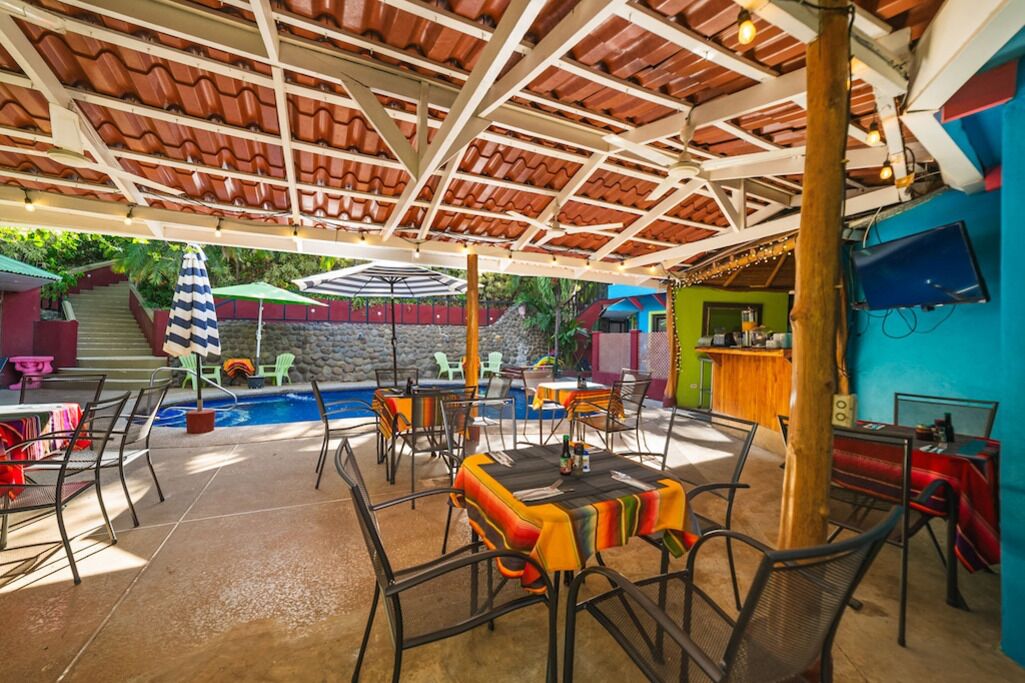 An outdoor patio area with tables and chairs, a pool, and a bar area.
