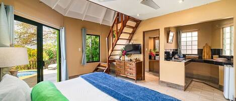 A spacious bedroom with a large bed, a desk area, and a staircase leading to an upper level.
