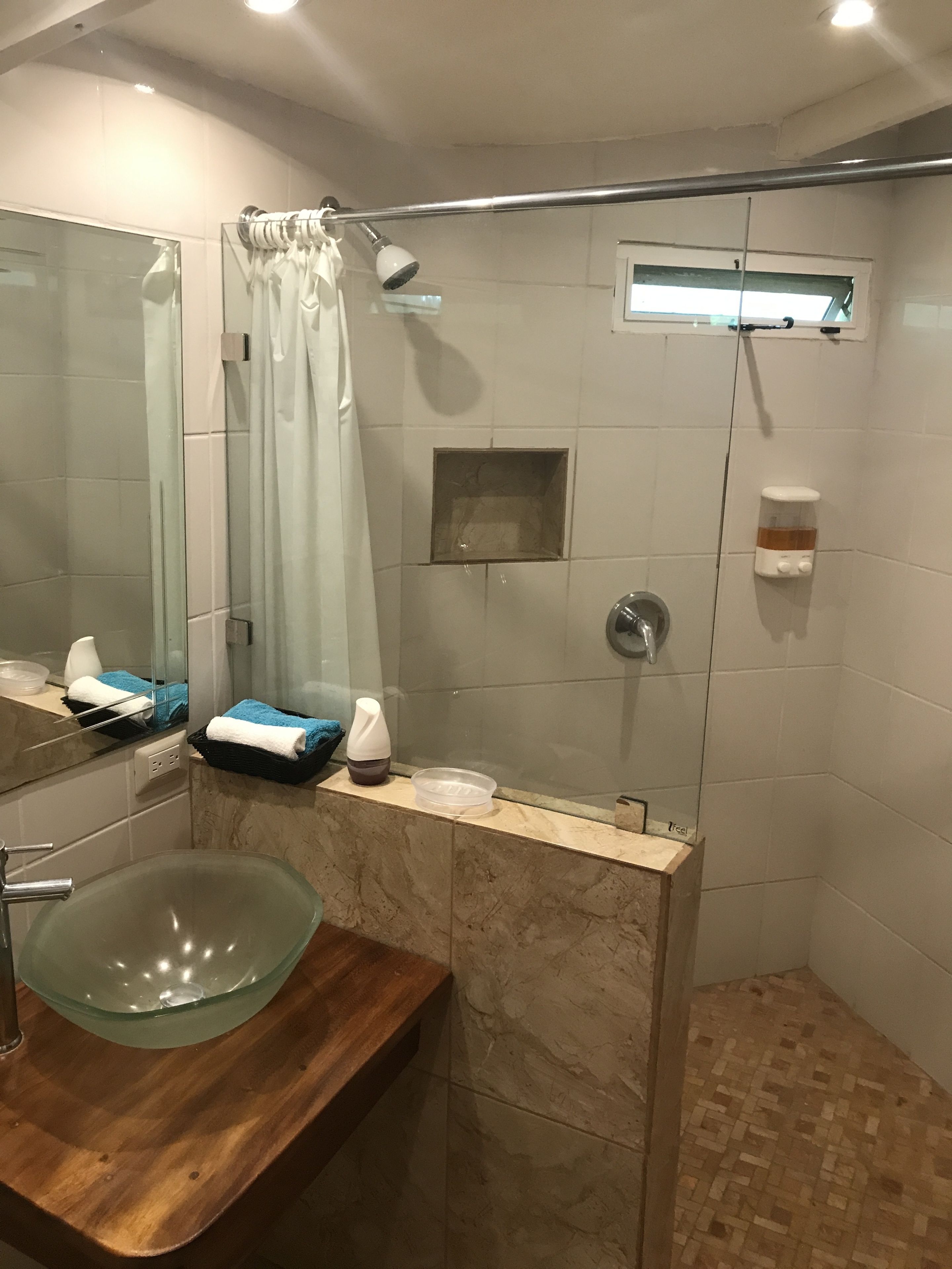 A modern bathroom with a glass sink, a shower with a glass door, and a vanity with a mirror.