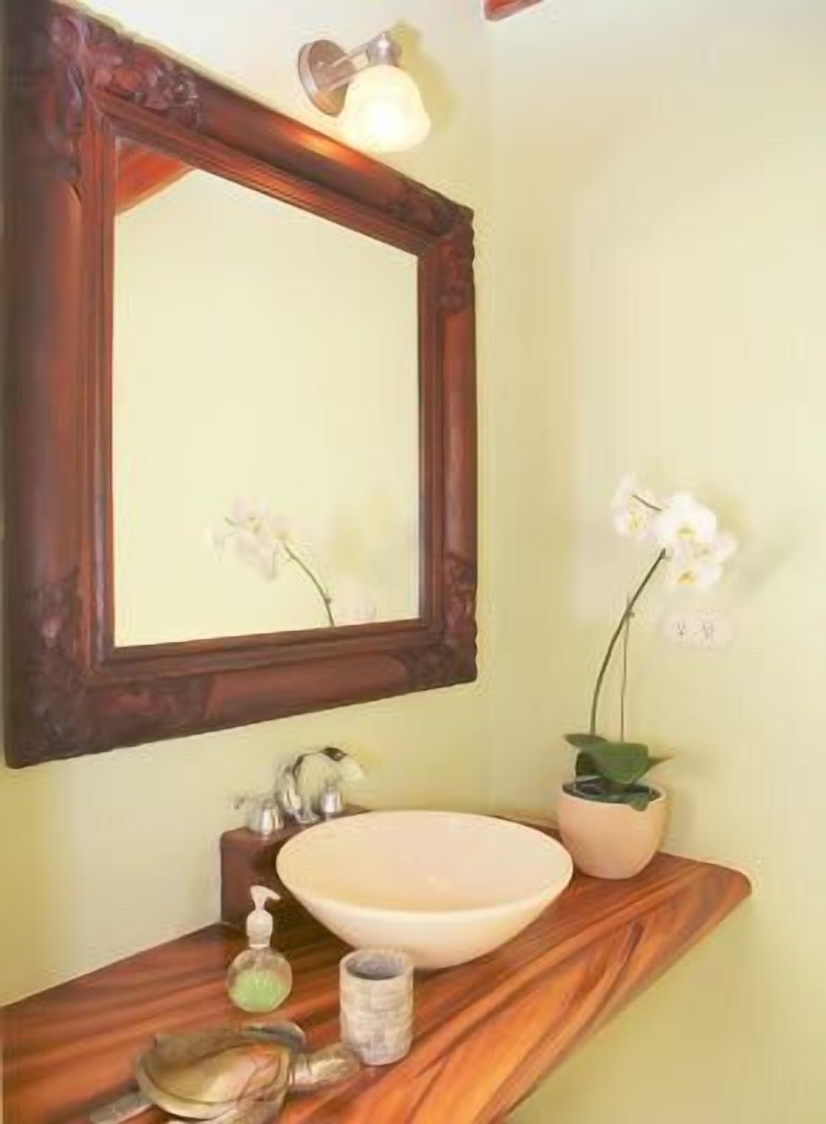 A bathroom with a wooden vanity, a large mirror, a sink, and two potted orchids.
