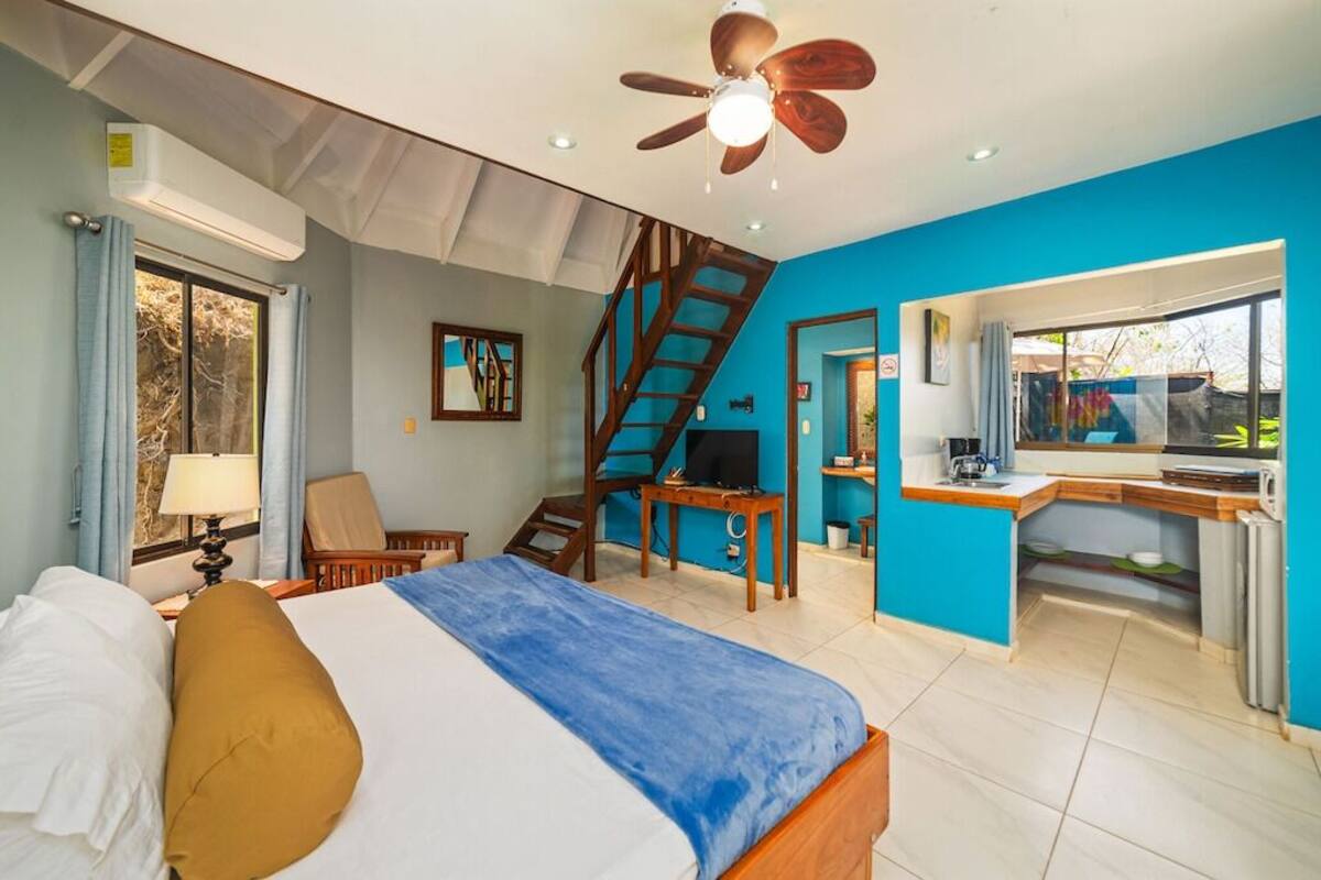 A bedroom with a bed, a desk, a chair, a television, and a staircase.