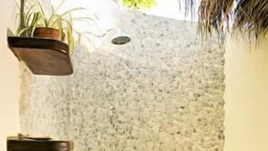 A stone wall with a built-in shower, a potted plant, and a chair. - Hotel Tamarindo Village (Tamarindo)