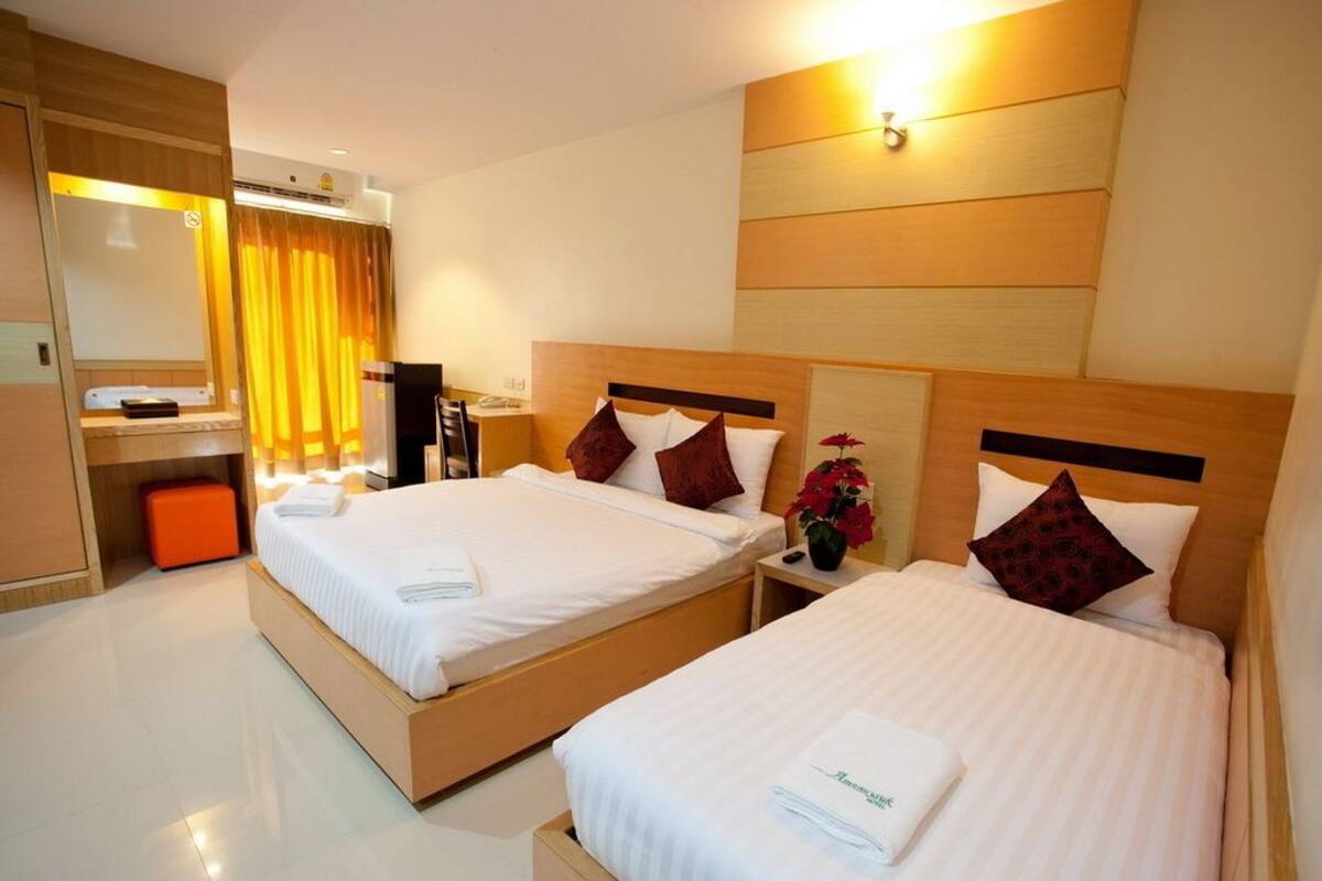 Une chambre d’hôtel avec deux lits, un bureau, une chaise, un miroir et un petit pouf orange.