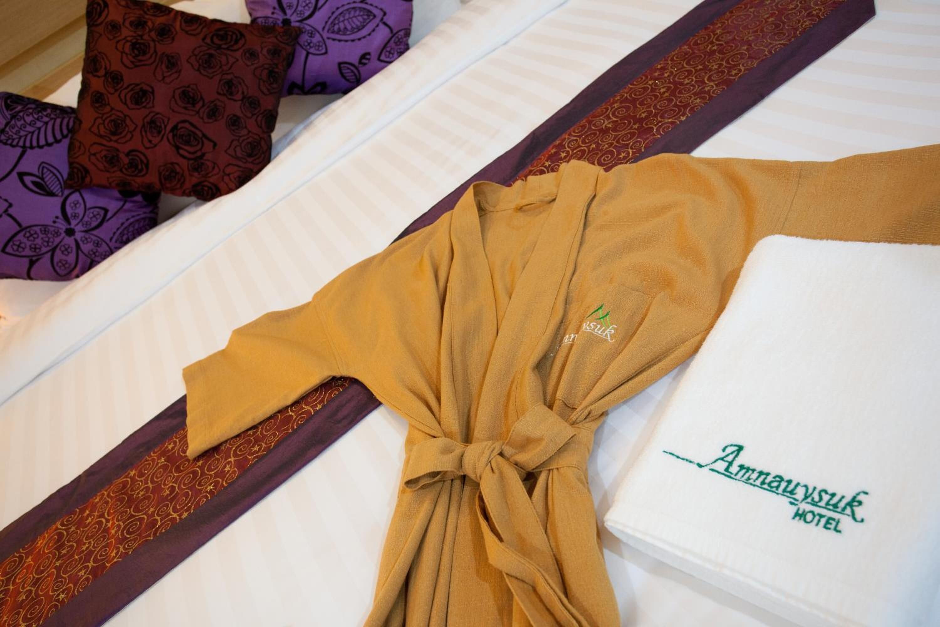 Una cama bien hecha con un albornoz marrón y una almohada blanca con el nombre 