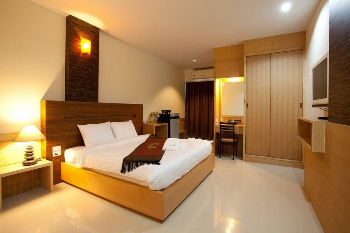 Une chambre d’hôtel moderne avec un lit en bois, une table de chevet avec une lampe, un bureau avec une chaise et un téléviseur fixé au mur.