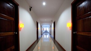 Un long couloir bien éclairé, avec des portes en bois et des lampes fixées aux murs.