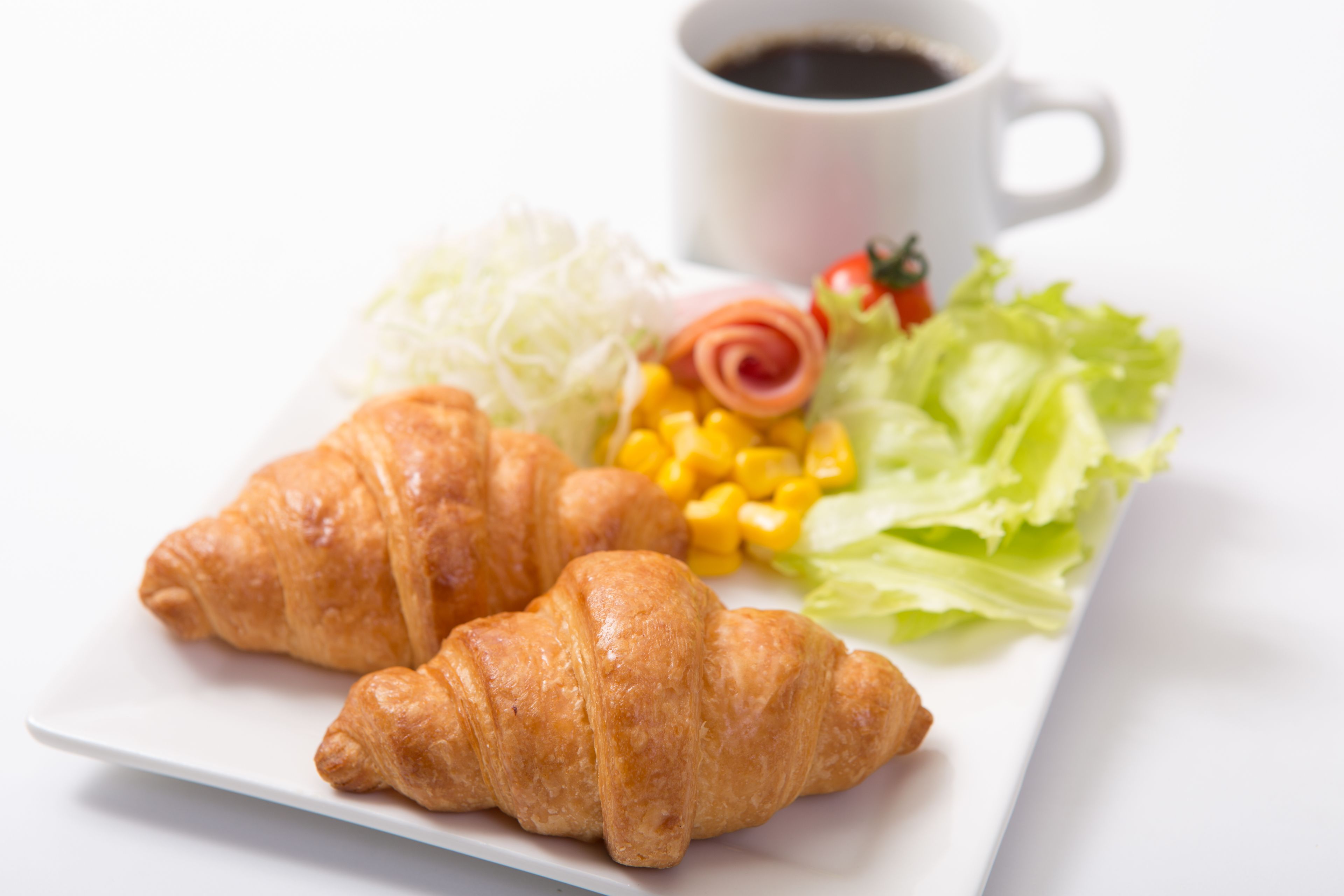 Un plato con cruasanes, una taza de café y una ensalada.