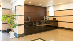 A reception area with a black reception desk, a potted plant, and a wooden panel wall. - Ariston Inn Kanda Kitakyushu Airport (Kanda)