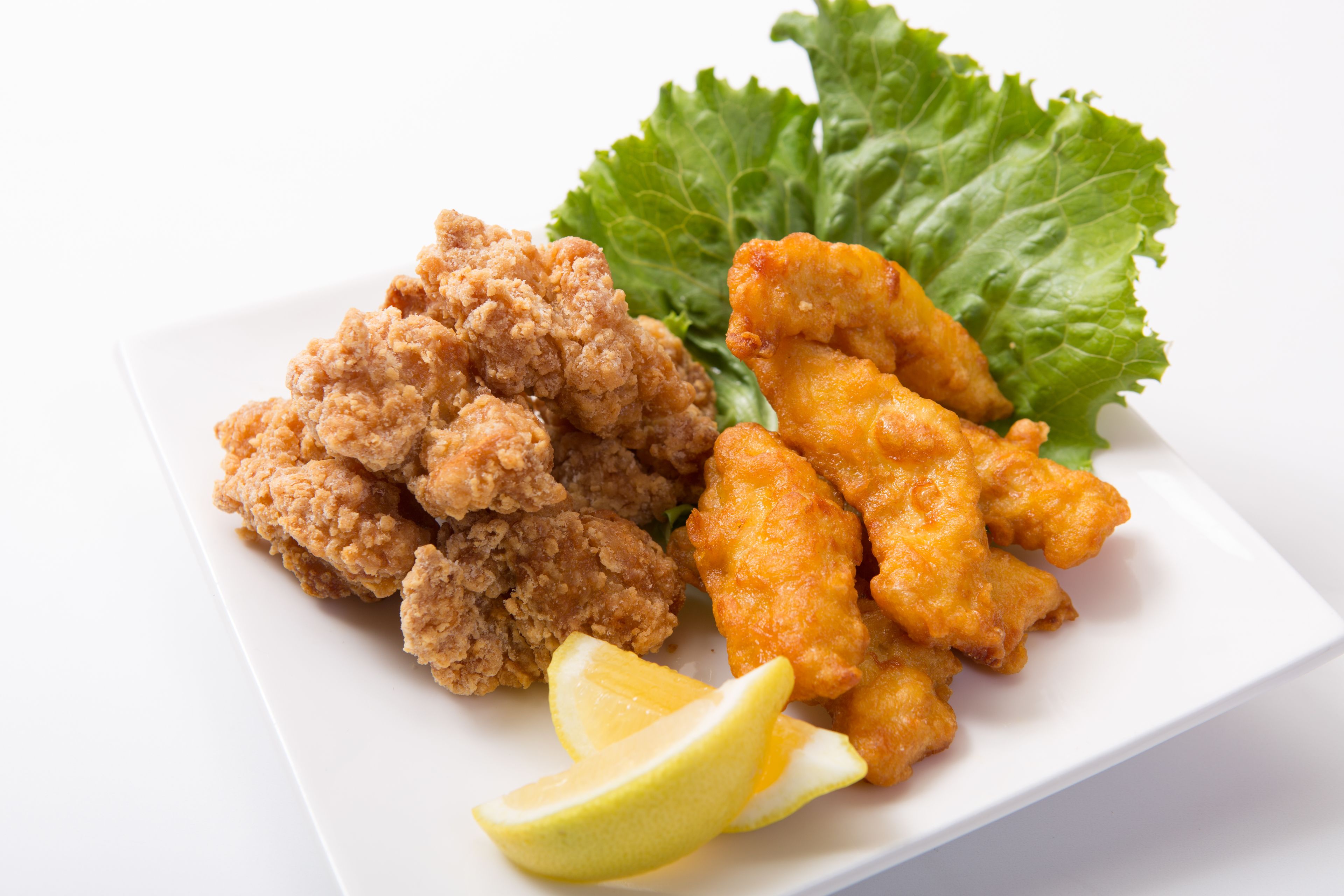 A plate of fried chicken and vegetables with a wedge of lemon.