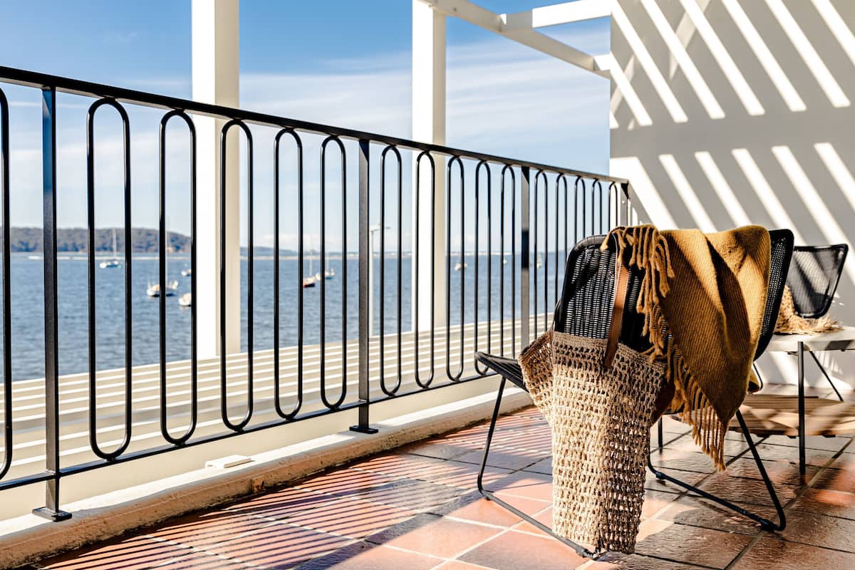 A balcony with a view of the water, a wicker chair, and a woven basket.