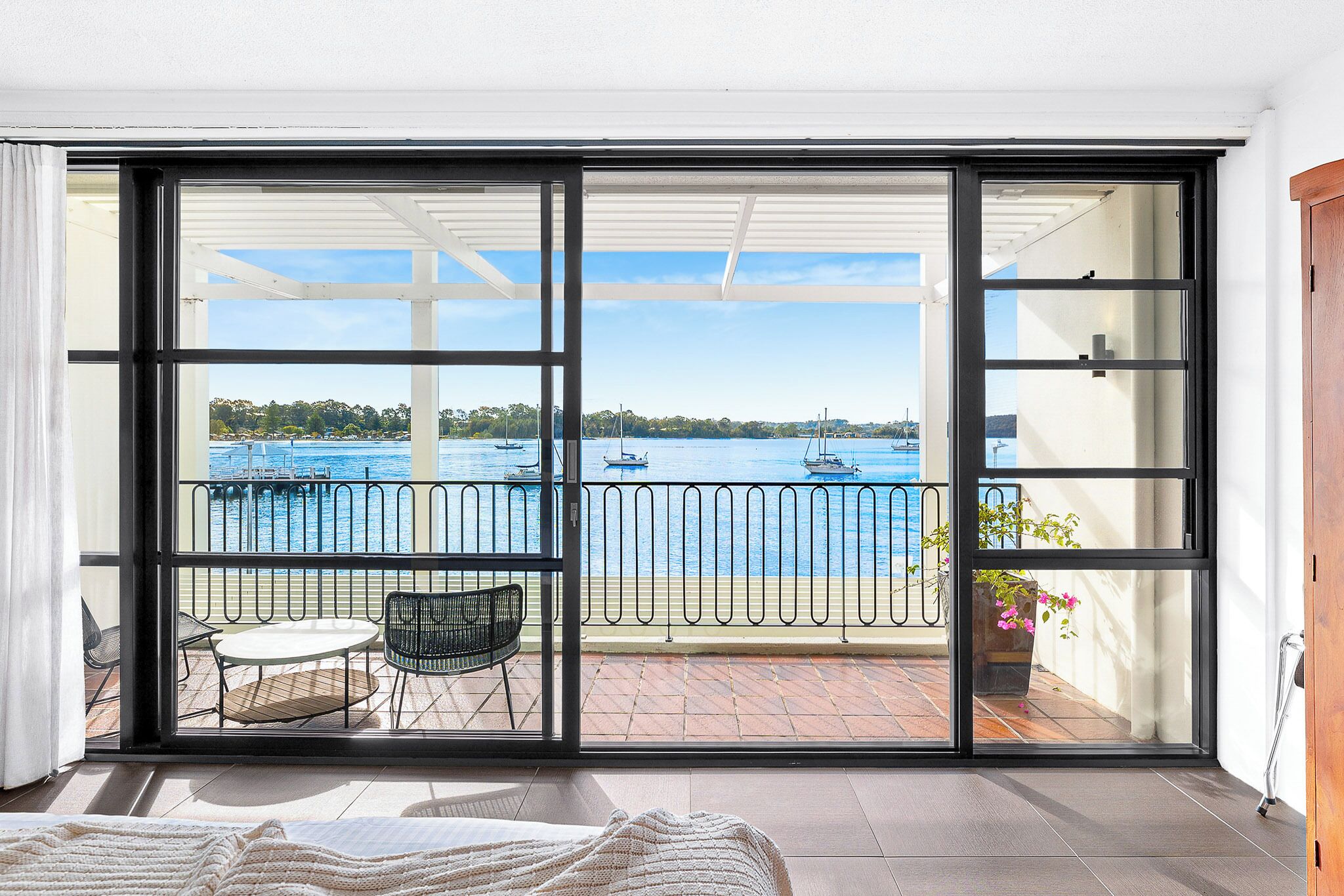Una stanza con un'ampia porta-finestra scorrevole che si apre su un balcone con vista sul mare e sulle barche.