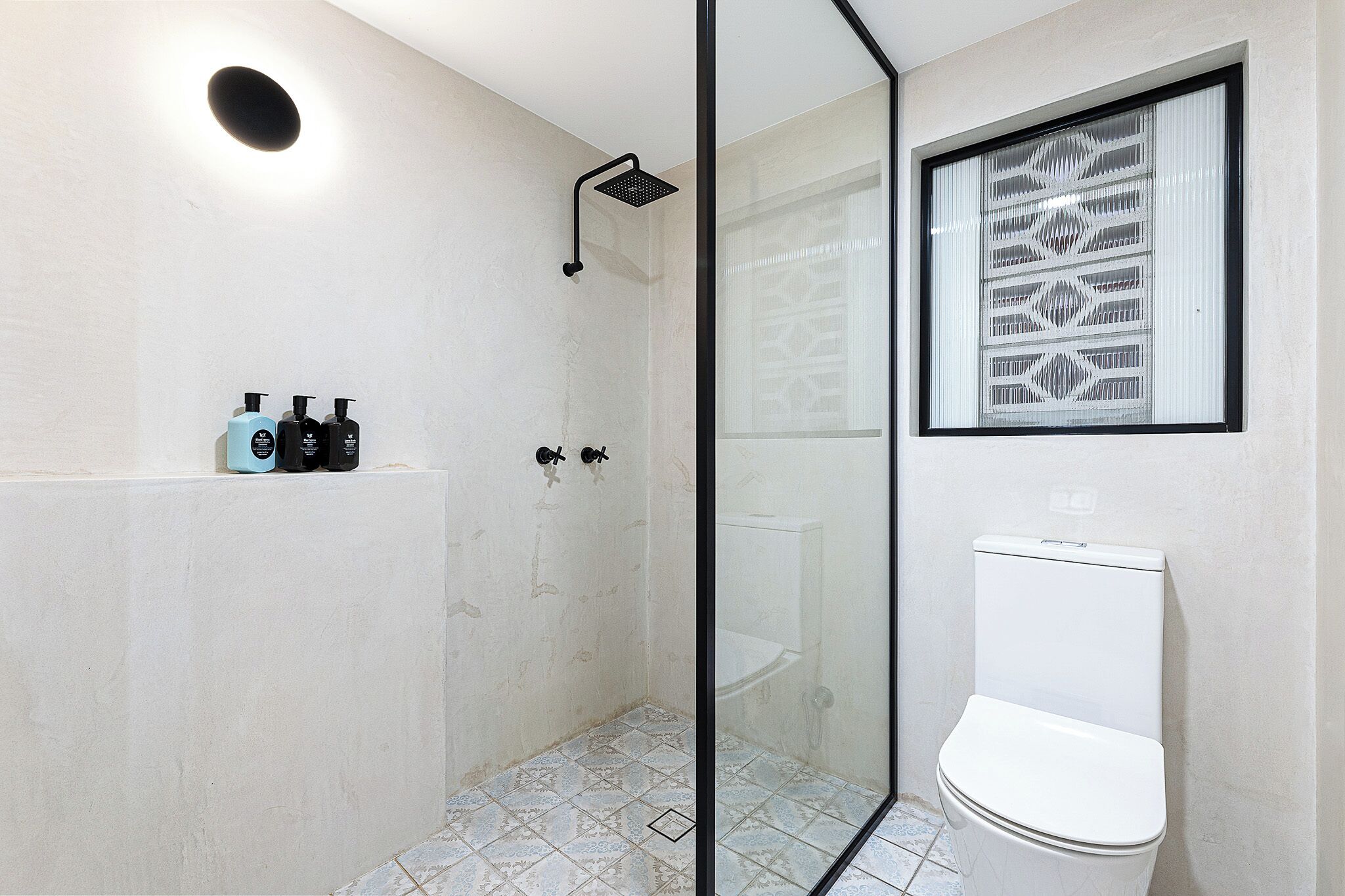 Un baño moderno con cabina de ducha de vidrio, inodoro y lavamanos adosado a la pared.