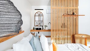 Une chambre moderne avec un lit, une cloison en bois, un fauteuil en osier et un luminaire suspendu.