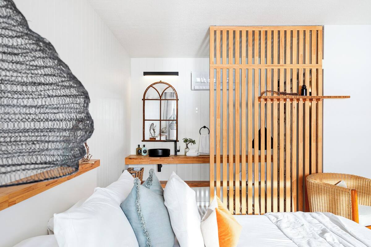 A modern bedroom with a bed, a wooden partition, a wicker chair, and a hanging light fixture.