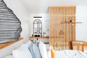 Un dormitorio moderno con cama, un separador de madera, una silla de mimbre y una lámpara colgante.