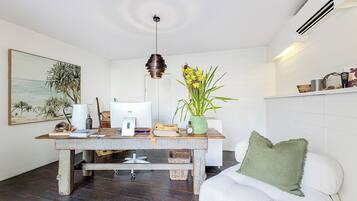 Una habitación con una mesa de madera, una lámpara colgante, un cuadro, una planta y un sofá blanco.