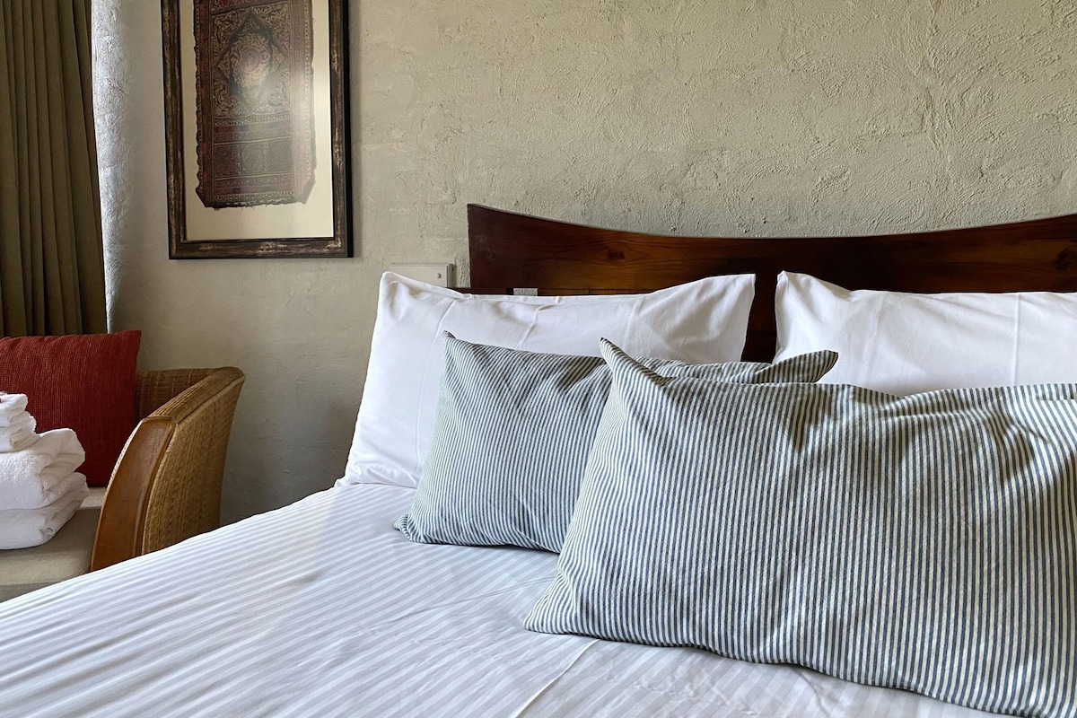 A neatly made bed with striped pillows, a wooden headboard, and a framed picture on the wall.