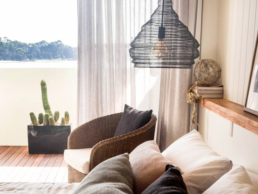 A balcony with a wicker chair, a potted cactus, and a hanging light fixture.