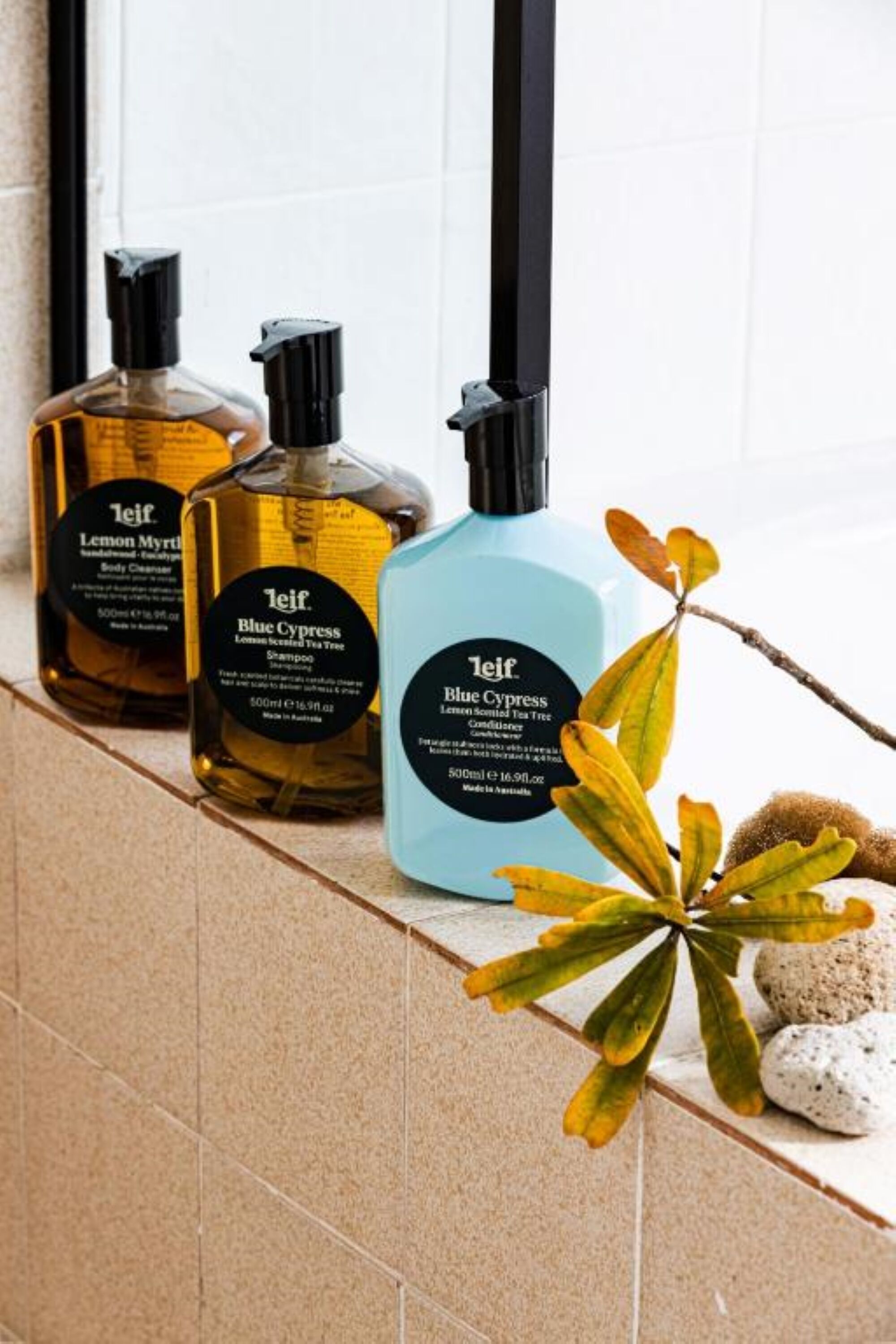 Three bottles of Leif Blue Cypress body care products on a tiled ledge.