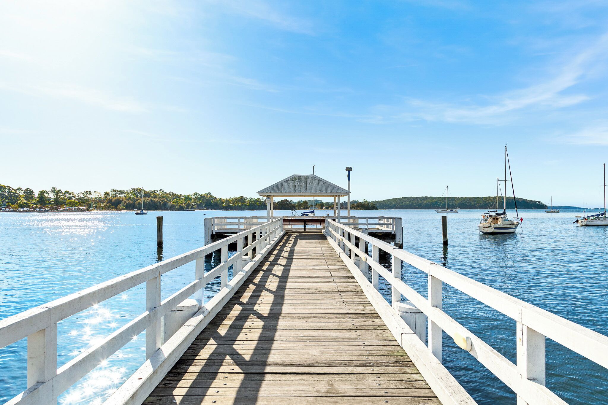 Eine hölzerne Pier führt zu einem Pavillon über dem Wasser, wo Boote liegen.