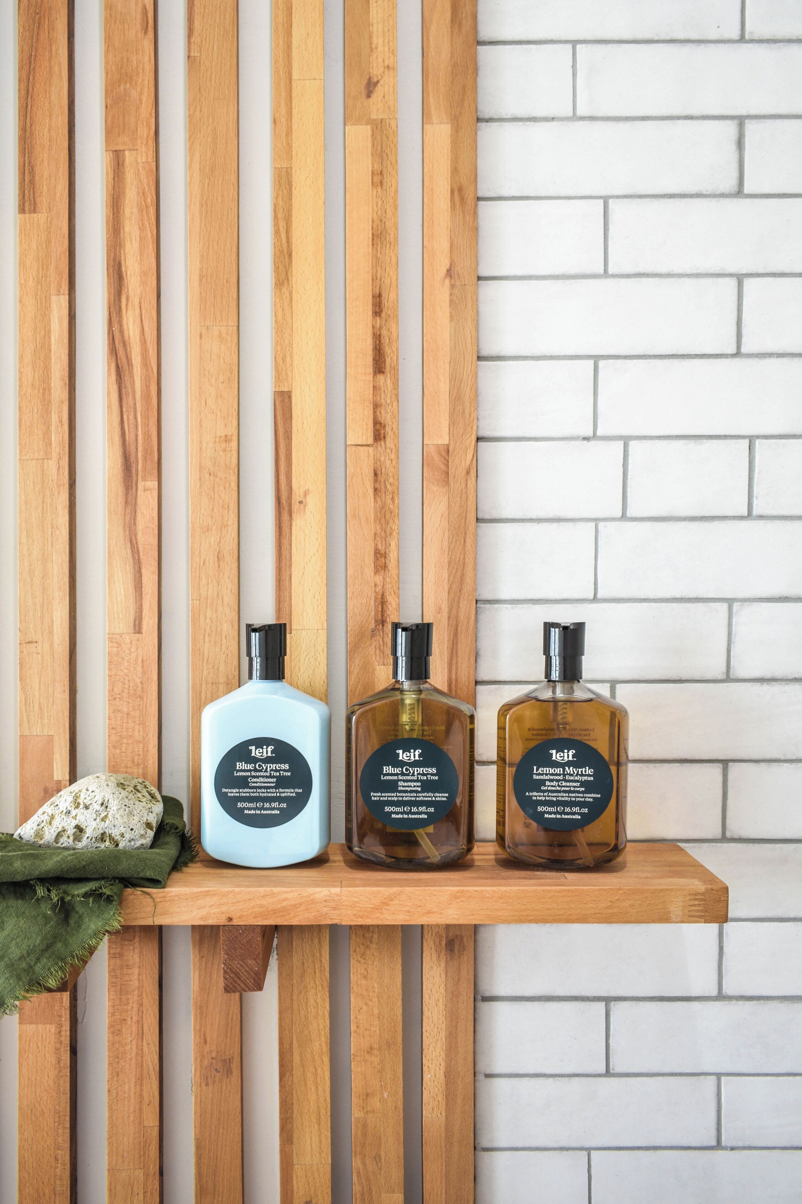 Tres botellas de productos de cuidado corporal Teifi sobre un estante de madera frente a una pared de ladrillo.