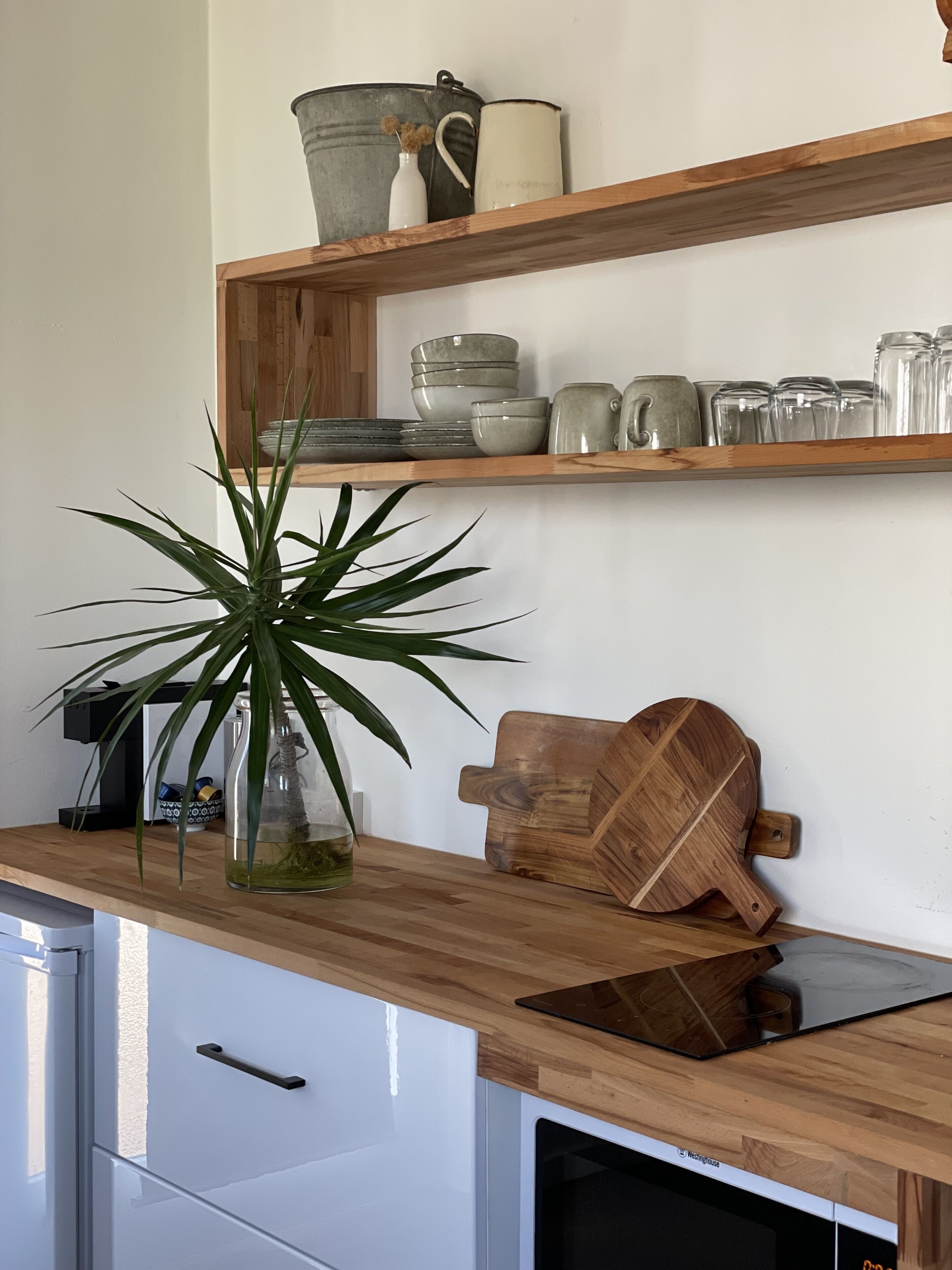 Une cuisine avec des étagères en bois où sont rangés divers ustensiles de cuisine, une plante en pot et une planche à découper en bois.