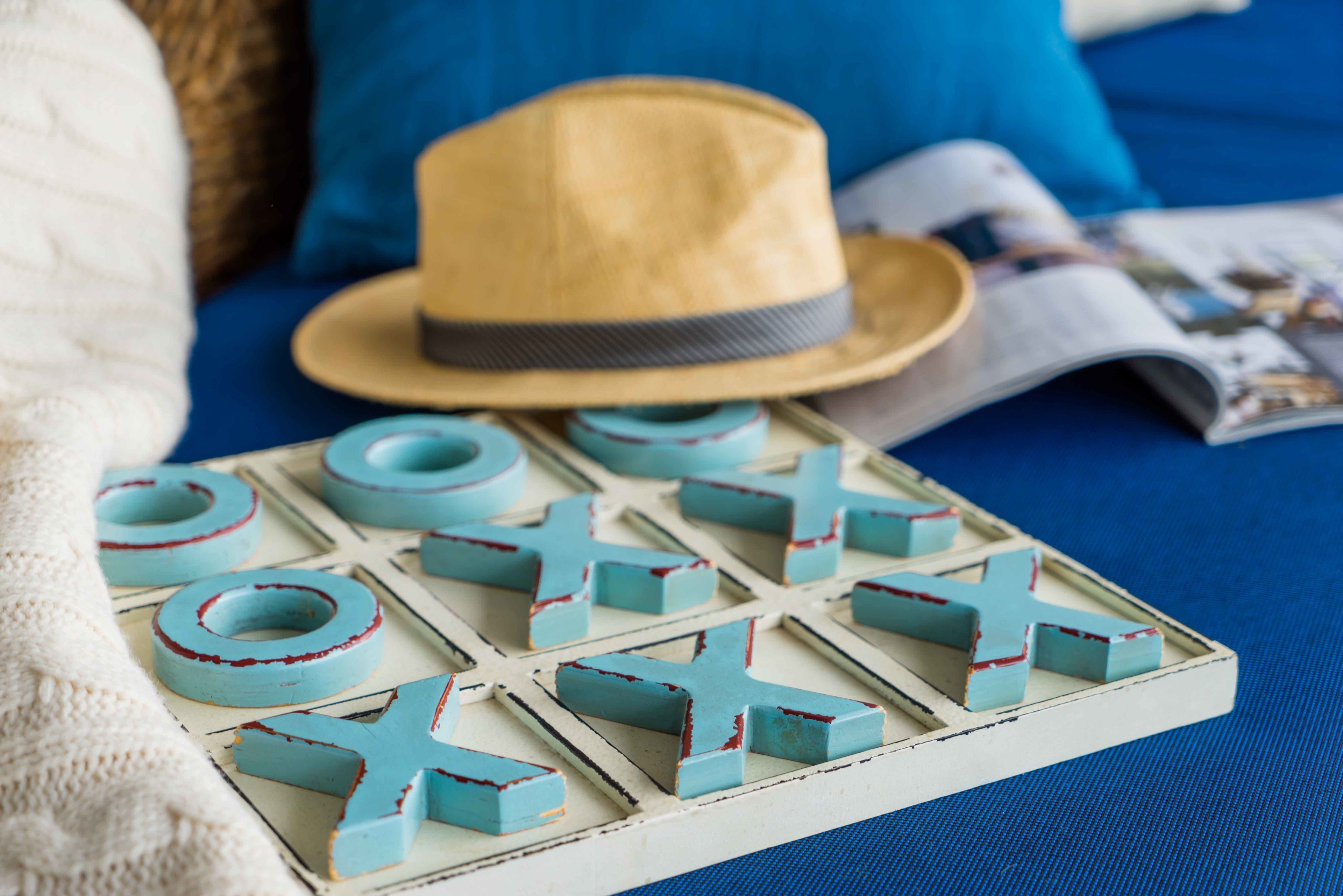 A board game with blue and red pieces, a straw hat, and a magazine on a blue surface.