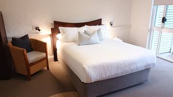 A hotel room with a large bed, a chair, a lamp, and a window.