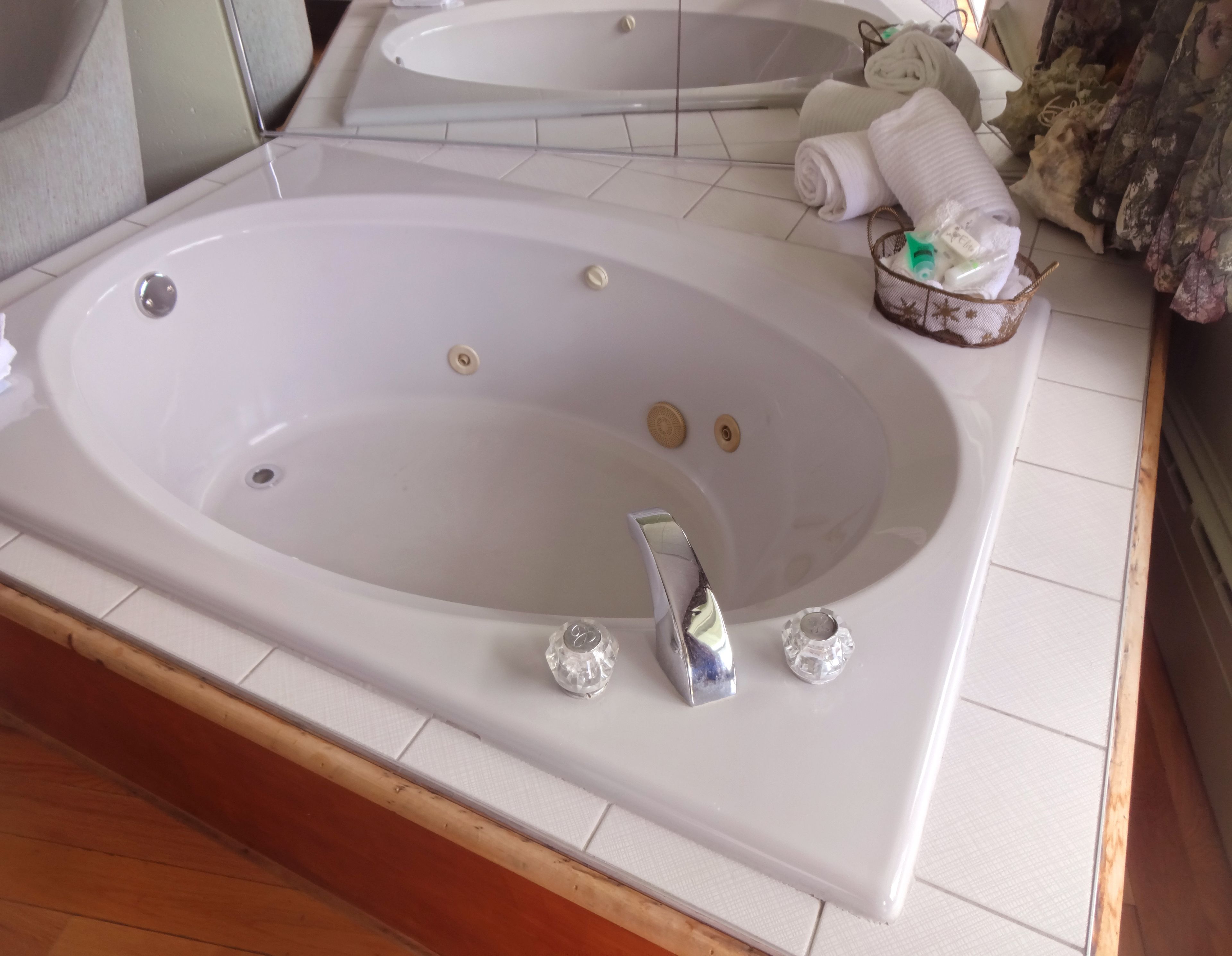 A bathroom with a large bathtub, a mirror, and a small basket with toiletries.