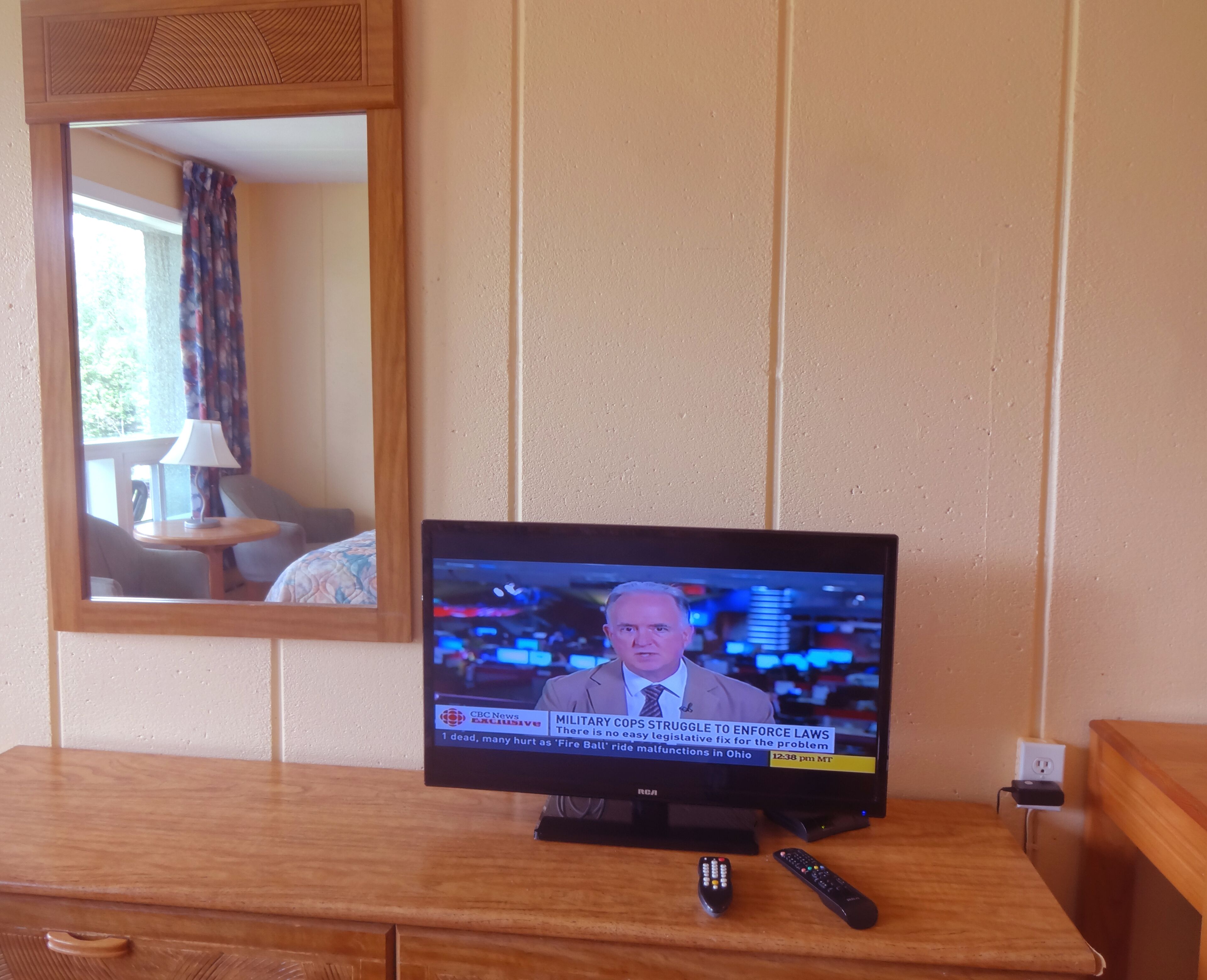 A television displaying a news program, a wooden dresser, and two remote controls.