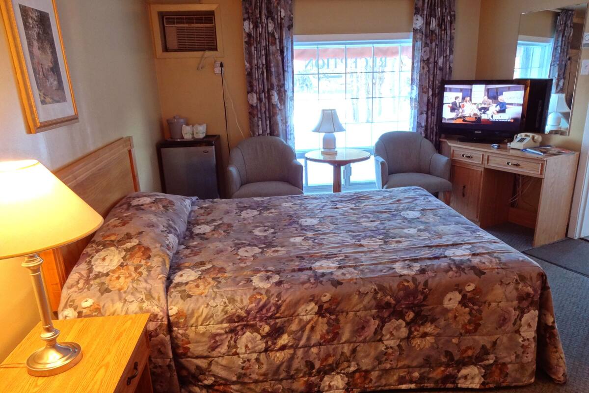 A hotel room with a bed, two armchairs, a small table, a television, and a desk with a lamp.