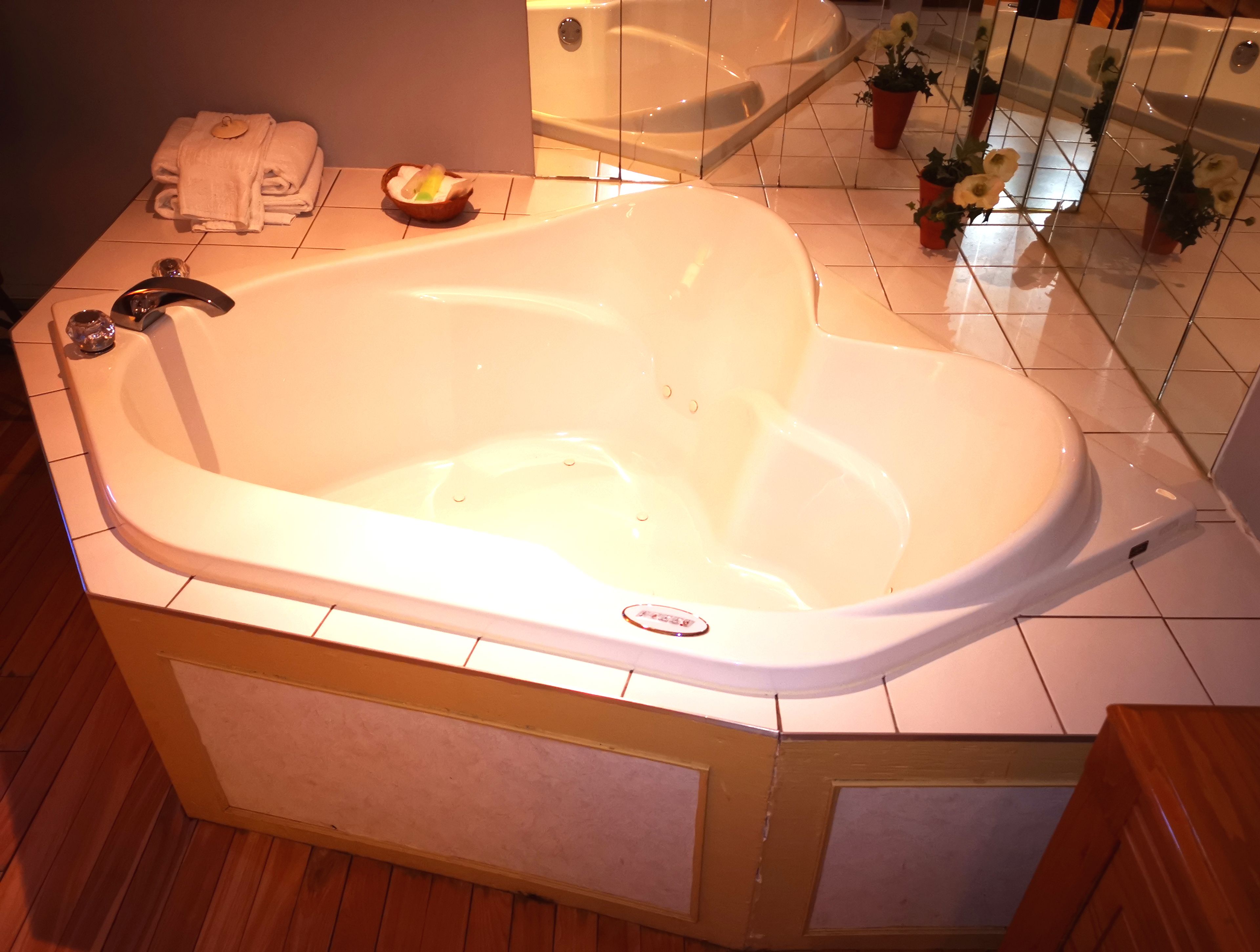 Una grande vasca da bagno bianca con una base in legno, un portasci con asciugamani piegati, una piccola ciotola e piante in vaso.