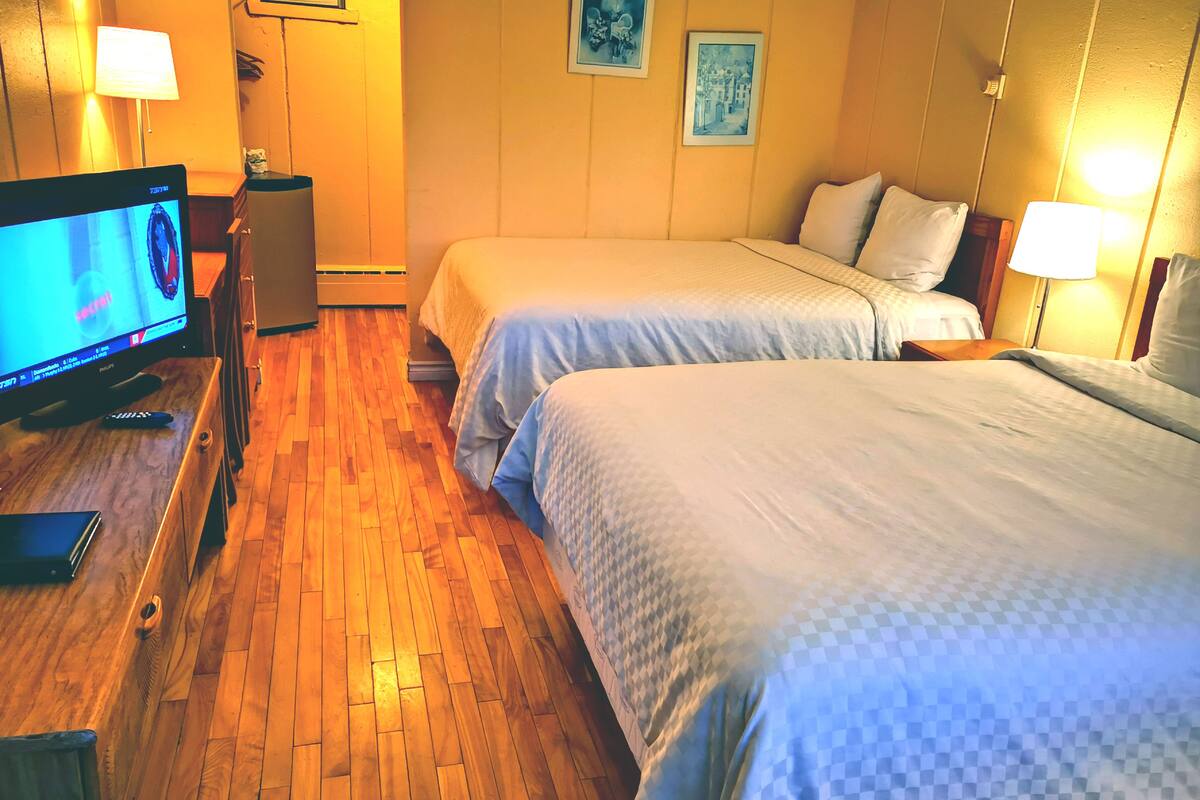 A hotel room with two beds, a television, and a desk with a laptop.