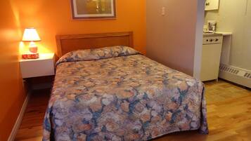 Un dormitorio con cubrecama floral, una mesita de noche con lámpara y una pequeña zona de kitchenette.